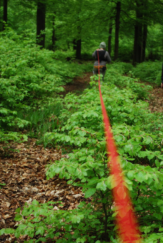 Eine Person läuft in den Wald und zieht einen langen roten Faden hinter sich her